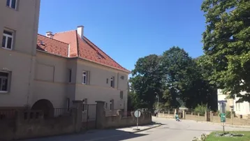 Gebäudeansicht von außen an einer Straßenecke mit Bäumen und blauem Himmel.