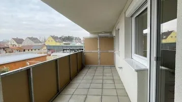 Langer Balkon mit Fliesenboden und Blick auf die umliegenden Häuser, ausgestattet mit Rollläden.