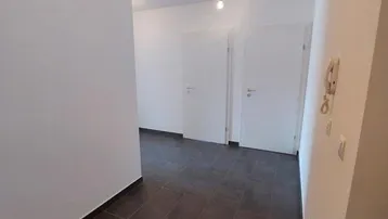 Heller Eingangsbereich mit dunklen Fliesen und weißen Türen, der zu weiteren Räumen führt.