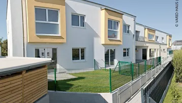 Mehrere moderne Reihenhäuser mit weißer Fassade und gelben Akzenten, umgeben von Grünflächen.