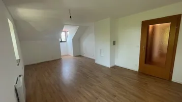 Heller Raum mit Holzboden, Dachschrägen und einem Fenster, ideal als Wohn- oder Schlafzimmer.