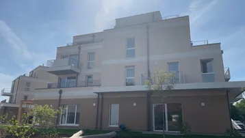 Modernes Mehrfamilienhaus mit beigefarbener Fassade, Balkonen und Grünflächen im Vordergrund.