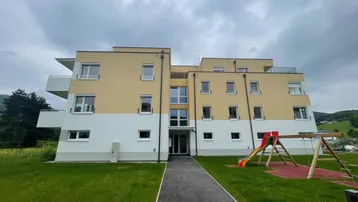 Modernes Mehrfamilienhaus mit gelb-weißer Fassade und Kinderspielplatz im Vordergrund.