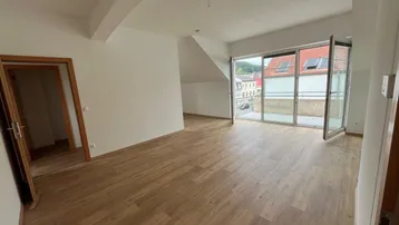 Helles Wohnzimmer mit Holzboden, Dachschrägen und Zugang zu einem Balkon mit Stadtblick.