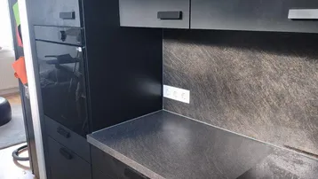 Moderne Küche mit schwarzen Schränken, dunkler Arbeitsplatte, integriertem Backofen und Induktionskochfeld.