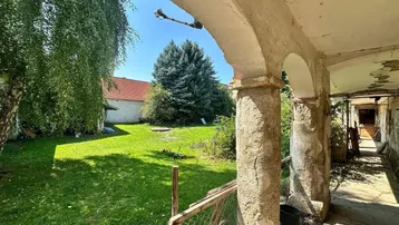 Alter, überdachter Gang mit Bögen und Blick auf den grünen Gartenbereich.