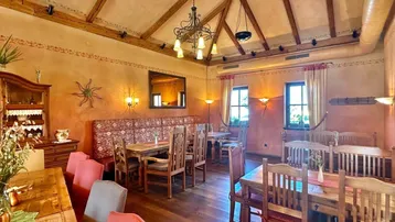 Rustikaler Speisesaal mit Holzbalkendecke, Holzboden und traditionellen Tischen und Stühlen.