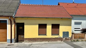 Altes, gelbes Haus mit rotem Ziegeldach und braunen Fensterläden, direkt an der Straße gelegen.