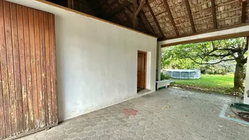 Überdachter Außenbereich mit gepflastertem Boden und sichtbarer Dachkonstruktion, angrenzend an den Garten.