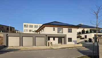 Modernes Neubau-Einfamilienhaus mit Doppelgarage und Photovoltaikanlage unter blauem Himmel.