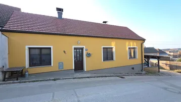 Gelb gestrichenes Einfamilienhaus mit rotem Ziegeldach und kleiner Veranda an der Vorderseite.