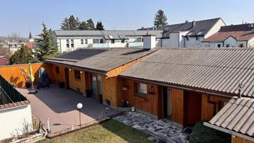 Hinterhof mit Holzterrasse, Rasenfläche und Blick auf die Umgebung.