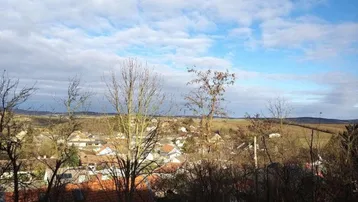 Weitblick über eine ländliche Siedlung mit vielen Häusern und bewaldeten Hügeln im Hintergrund.