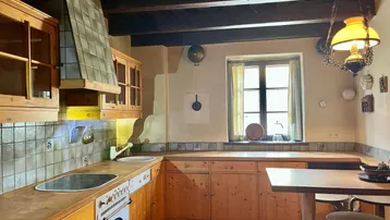Traditionelle Holzküche mit sichtbaren Deckenbalken, Holzschränken und einem kleinen Esstisch.