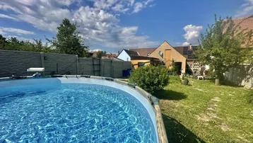 Großer Garten mit einem Aufstellpool und viel Grünfläche unter blauem Himmel.