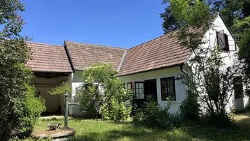 Weißes Landhaus mit traditionellem Ziegeldach, umgeben von üppigem Grün und einem alten Brunnen im Garten.