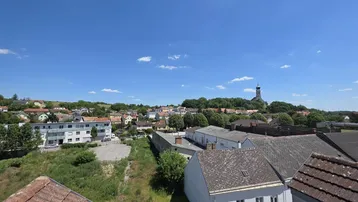 Weitläufiger Blick über die Dächer der Stadt und die umliegende Landschaft mit Kirche.
