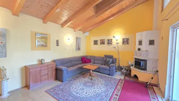 Geräumiges Wohnzimmer mit Holzbalkendecke, Kachelofen und einer gemütlichen Sitzecke.