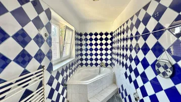 Badezimmer mit auffälligen blau-weißen Fliesen, einer Eckbadewanne und einem Fenster.