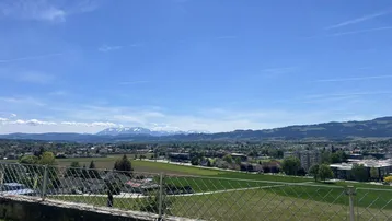 Weitläufiger Panoramablick über die Landschaft mit Bergen im Hintergrund unter einem klaren blauen Himmel.
