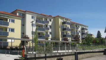 Mehrfamilienhaus mit mehreren Balkonen und moderner Architektur unter blauem Himmel.