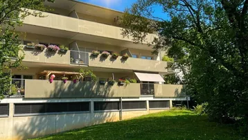 Mehrfamilienhaus mit mehreren Balkonen und grüner Rasenfläche an einem sonnigen Tag.