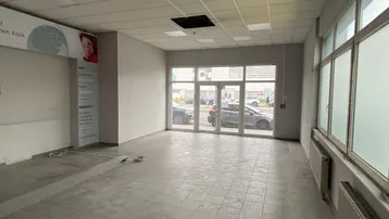Leerer Gewerberaum mit großen Schaufenstern zur Straße, Fliesenboden und abgehängter Decke.