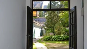 Blick durch große offene Türen auf einen grünen Gartenbereich mit Bäumen.