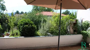 Terrasse mit Sonnenschirm und üppiger grüner Bepflanzung, bietet einen ruhigen Außenbereich.