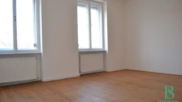 Heller Raum mit Holzdielenboden, weißen Wänden und zwei großen Fenstern.