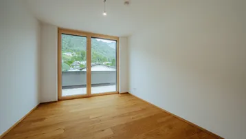 Helles Schlafzimmer mit Holzboden und Balkonzugang, bietet einen schönen Blick auf die grüne Berglandschaft.