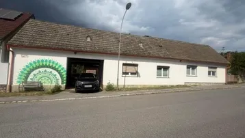 Langes, weißes Gebäude mit Ziegeldach und einem Auto in der offenen Garage.