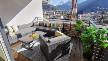 Möblierter Balkon mit Holzboden, gemütlicher Sitzecke und beeindruckendem Bergblick.