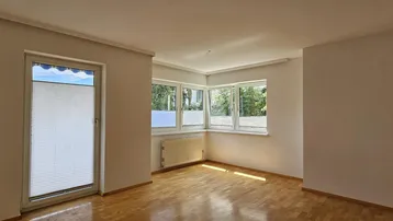 Helles Zimmer mit Parkettboden und großen Fenstern, die viel Tageslicht hereinlassen und einen Zugang nach draußen bieten.