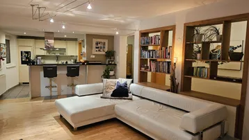 Offener Wohnbereich mit weißem Sofa, Holzboden und integrierter Küche mit Frühstücksbar.