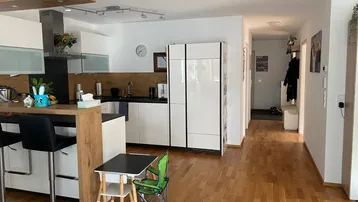 Moderne Küche mit Frühstücksbar, weißen Schränken und offenem Zugang zum Flur.