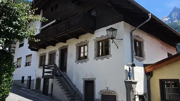 Traditionelles alpines Haus mit weißer Fassade, Holzbalkonen und Bergblick in sonniger Lage.