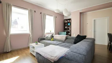 Gemütliches Wohnzimmer mit großem Ecksofa, hellrosa Wänden und Holzboden, ideal zum Entspannen.