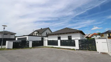 Modernes Einfamilienhaus mit weißer Fassade, dunklem Dach und dekorativem Zaun.