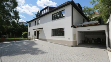 Modernes Mehrfamilienhaus mit weißer Fassade, gepflasterter Auffahrt und integrierter Garage.