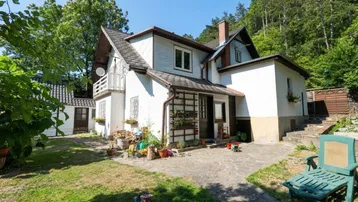 Charmantes Einfamilienhaus mit großem Garten und gepflastertem Bereich, umgeben von viel Grün.