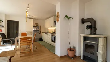 Gemütlicher Wohnbereich mit Kachelofen und offenem Übergang zur modernen Küche.