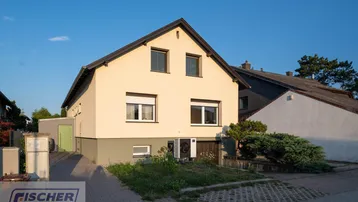 Gelbes Einfamilienhaus mit Satteldach und kleiner Auffahrt bei Sonnenuntergang.