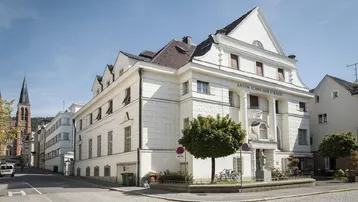 Historisches Gebäude an einer Straßenecke mit weißer Fassade und Blick auf einen Kirchturm.