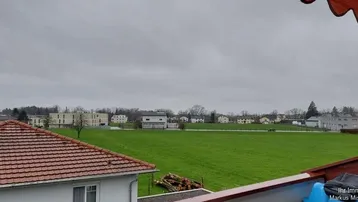 Weitblick über grüne Felder und Dächer von einem Balkon aus.