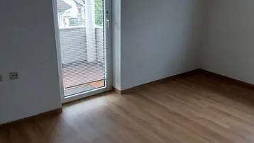 Helles Zimmer im Dachgeschoss mit Laminatboden und Zugang zu einem kleinen Balkon.