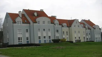 Reihenhausanlage mit hellen Fassaden, roten Ziegeldächern und Gaubenfenstern, umgeben von einer gepflegten Grünfläche.