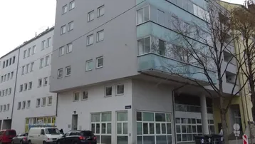 Modernes Mehrfamilienhaus mit grauer Fassade und großen Glasfronten in städtischer Umgebung.
