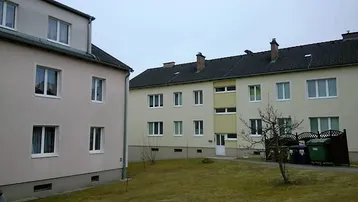 Zwei Mehrfamilienhäuser mit hellen Fassaden, weißen Fenstern und einem gemeinsamen Rasenbereich im Vordergrund.