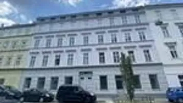 Die Fassade eines gepflegten Altbaus mit zahlreichen Fenstern und parkenden Fahrzeugen auf der Straße.